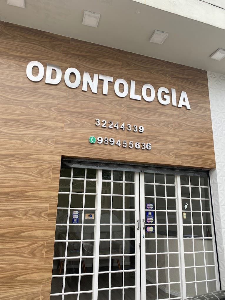 Fachada do consultório, com o letreiro ODONTOLOGIA em letras de aço sobre o painel de madeira e a porta de vidro
